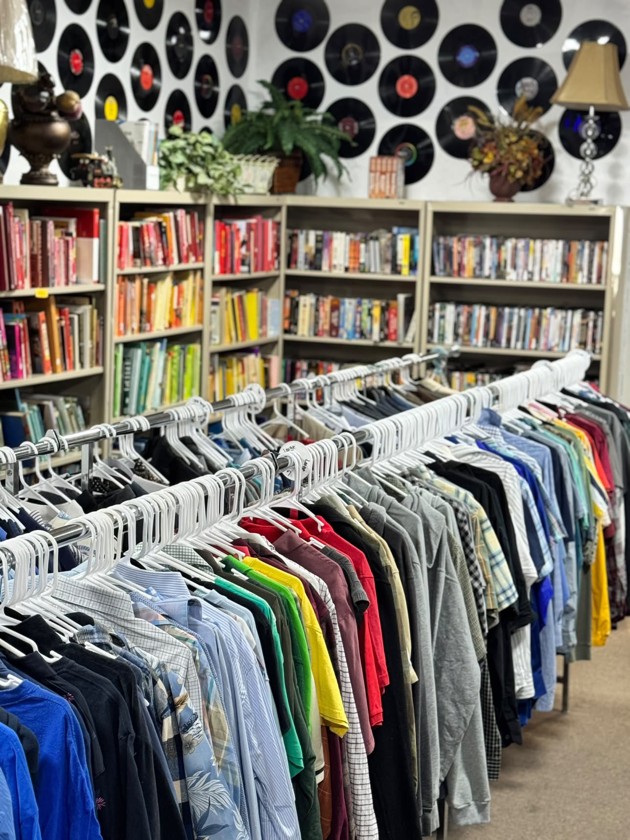 Rows of clothing on racks with shelves of books and records